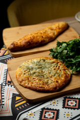 Two varieties of flatbread sit on wooden boards, showcasing a golden crust and melted cheese. Fresh herbs accompany them, adding a touch of vibrant green to the scene