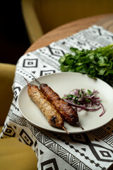 Two delicious skewers of grilled meat are placed on a round plate, accompanied by sliced red onions and fresh cilantro. The cozy atmosphere adds warmth to the meal