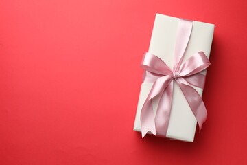 Beautiful gift with bow on red background, top view. Space for text