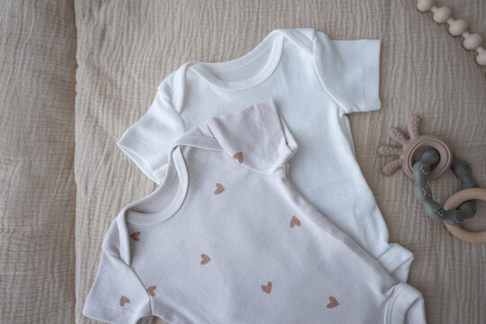 Composition with white baby clothes, accessories and toys on brown background. Newborn bodysuits. Baby essentials and motherhood concept