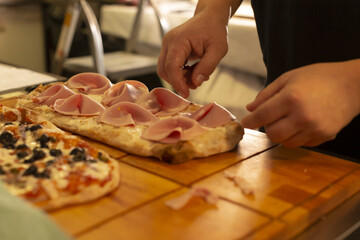 cook finishing pizza at service pass, hands adjusting ham and cheese before plating, warm counter glow, focused pace for outgoing