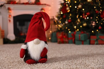 Fototapeta premium Cute Christmas gnome on floor against blurred lights indoors, closeup. Space for text