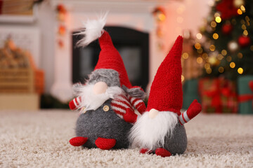 Fototapeta premium Cute Christmas gnomes on floor against blurred lights indoors, closeup