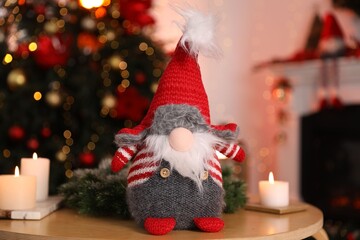 Fototapeta premium Cute Christmas gnome, burning candles and wreath on wooden table against blurred lights indoors, closeup