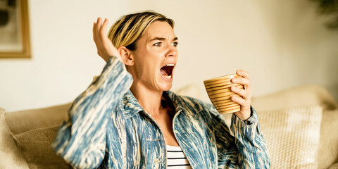Woman feeling shock and frustration, expressing a strong reaction after a clumsy moment, spilling a drink on the couch
