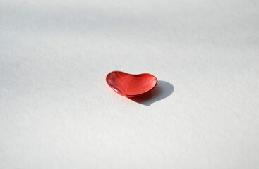 A small red heart with a few drops of water on the surface, creating a feeling of freshness and tenderness, lies on a white background. A declaration of love and feelings.