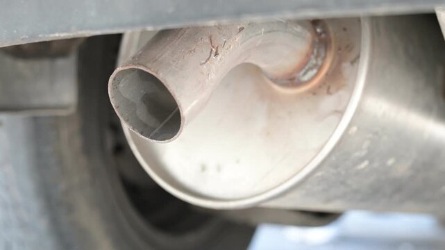 Close-up of a car exhaust pipe shaking slightly while the engine idles, with low-frequency rumble and subtle vibrations coming from the muffler in a stationary vehicle