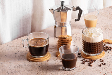 Freshly brewed espresso, iced coffee and moka pot in beige cozy kitchen setup. Different types of coffee drinks with cookies on a beige table