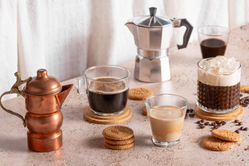 Freshly brewed espresso, iced coffee and two moka pots in beige cozy kitchen setup. Different types of coffee drinks with cookies on a beige table