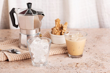 Iced coffee, espresso cups with ice and moka pot on textured beige stone table