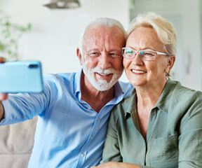 Portrait of a happy senior couple taking a selfie embracing hugging and having fun at home
