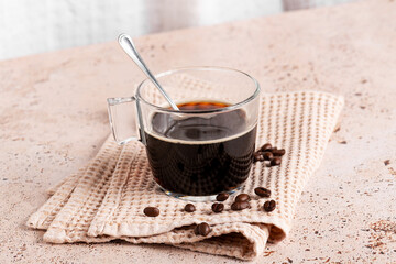Fresh brewed black coffee with scattered beans on textured napkin on beige stone kitchen table, Coffee break, refreshing energy drink