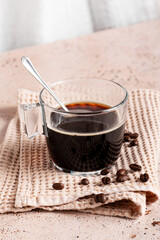 Glass cup of strong soluble black coffee on waffle cloth with roasted coffee beans on textured napkin on beige stone kitchen table, Coffee break, refreshing energy drink