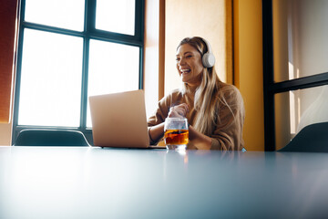 Young woman in headphones working on a project using a laptop in creative office