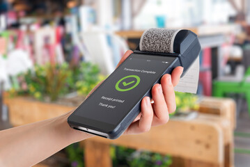 Hand holding POS terminal in store environment, showing completed payment with green checkmark and printed receipt during retail checkout