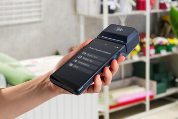 Hand holding POS terminal in store, showing payment method options including credit card, mobile pay, contactless and cash