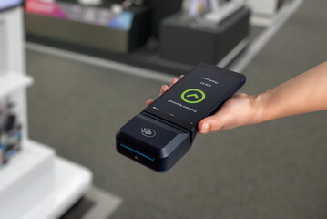 Hand holding POS terminal in electronics store, showing payment approved screen during digital checkout and cashless transaction process