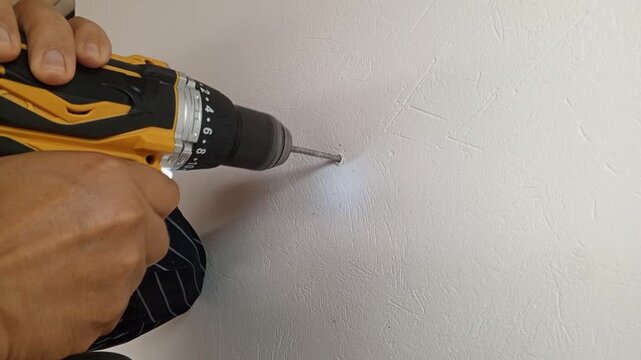 Unrecognizable man drilling a hole in a white wall using a cordless electric drill. Household tools