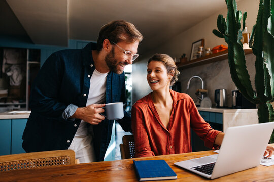 A couple chatting at the kitchen table with a laptop - Powered by Adobe