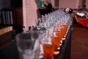 Celebratory drink scene, Orange liqueur shots at bar, Bartender pours drinks amidst lively party ambiance, Glassware reflects warm light during festive celebration at bar