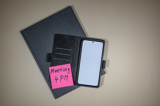 Notizbuch und Mobiltelefon mit Notizzettel "Meeting 4 PM"