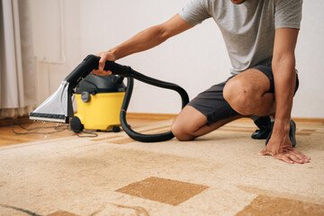 Close-up of cleaning service worker using washing vacuum cleaner to remove dirt and dust from...