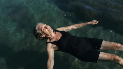 Elderly woman with serene mood floating on calm seawater against dark ocean background with copy space