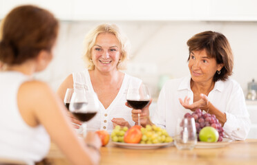 Girlfriends chatting and drinking wine at home party table in kitchen