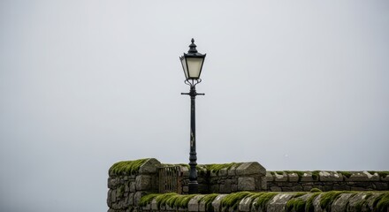 Vintage street lamp on moss-covered stone wall under cloudy sky