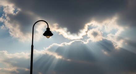 Street lamp under dramatic cloudy sky with sun beams breaking through
