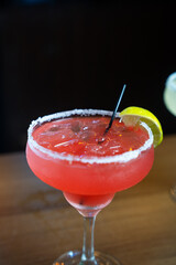 Strawberry frozen margarita cocktail with salt rim and lemon garnish
