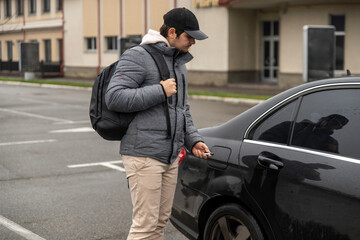 Young man opening black car on parking lot