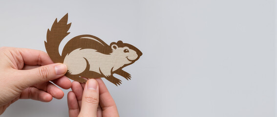 Hands holding groundhog cutout on gray background with detailed features highlighting playful expression. Groundhog cutout symbolizes fun and creativity for seasonal celebrations or events.