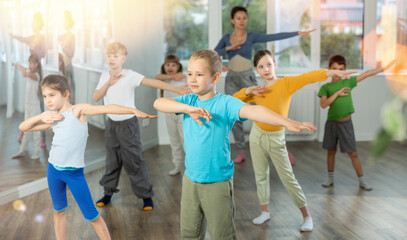 Positive juvenile boy engaged in hip-hop dance together with children's group and female trainer in training room