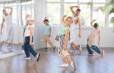 Preteen girl performing hip hop dance moves, showcasing skills and concentration, during group class for kids led by young male instructor in street dance studio..
