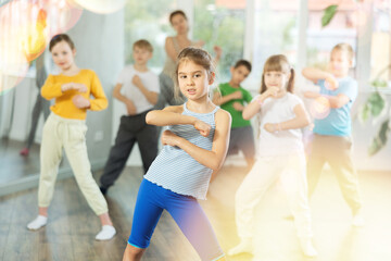 Girls with boys repeat teaches sequences of movements during training, train to perform electro dance, enjoys active hobby to favorite music. Unrecognizable female teacher administer conduct class