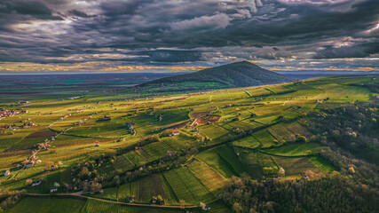 Sunlit aerial view of vineyards and fields around Hill, dramatic clouds and glowing patterns across the landscape.