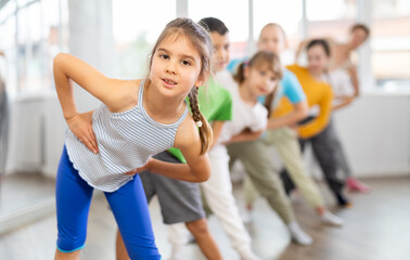 Positive juvenile girl engaged in choreography exercises together with children's group