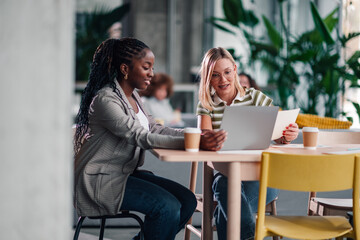 Diverse businesswomen collaborating using laptop and documents in office