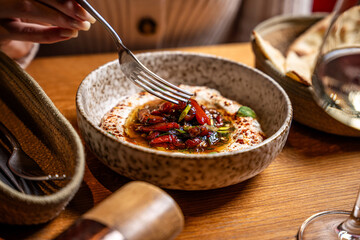 Hand serving marinated peppers with tzatziki in restaurant setting