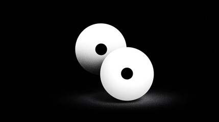 Two white spheres with black circles rest on a dark surface.