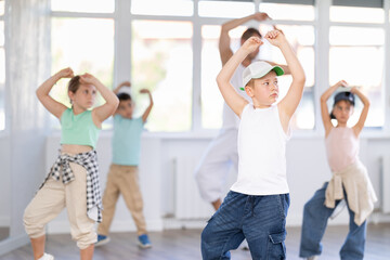 Young happy boy and group of positive children practicing energetic hip hop movements at modern dance school