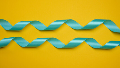 Blue satin ribbon, curved into a wave, centered on a yellow background. Concept for gift, decoration, and celebration.