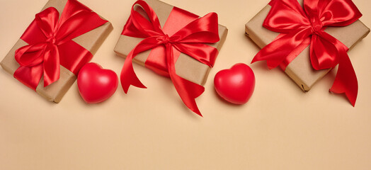 Gifts wrapped in red satin ribbon with a bow on a beige background