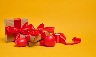 Gifts wrapped in brown paper and red satin ribbon on a yellow background, holiday