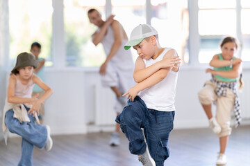 Obraz premium Preteen boy performing hip hop dance moves, showcasing skills and concentration, during group class for kids led by young male instructor in street dance studio