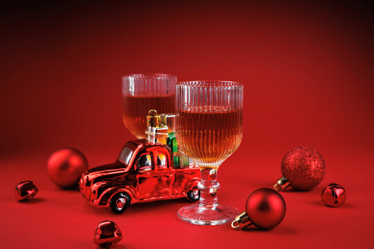 Two whiskey glasses with red toy car carrying gifts and Christmas ornaments on festive red background - Powered by Adobe