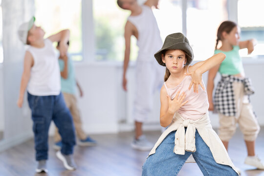 Emotional tween girl mastering krump dance routines during lively group session in children dance studio, guided by passionate male teacher..