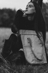 Atmospheric Black and White Portrait of a Woman Sitting on the Grass with a Large Ecological Tote Bag At a Tree Trunk in the Shadowy Forest