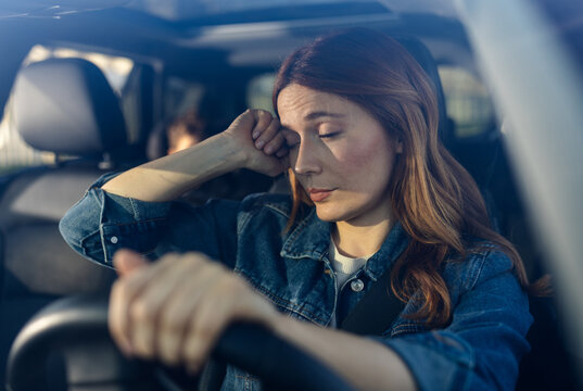 Woman sits in car looking worried and tired